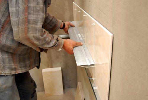 Проверяем ровно ли уложена плитка алюминиевой рейкой